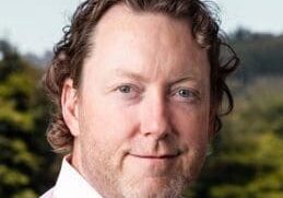Portrait of a middle-aged man with curly hair outdoors.