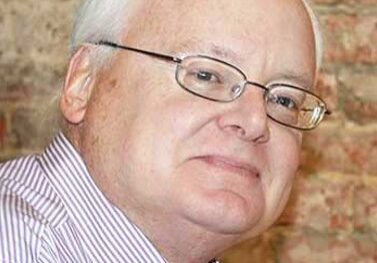 Portrait of an elderly man with glasses smiling gently.