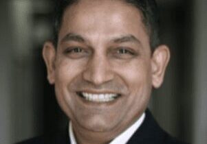 Smiling man in a dark suit and white shirt.