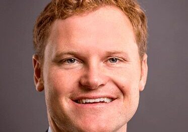 Smiling man with red hair in a suit.