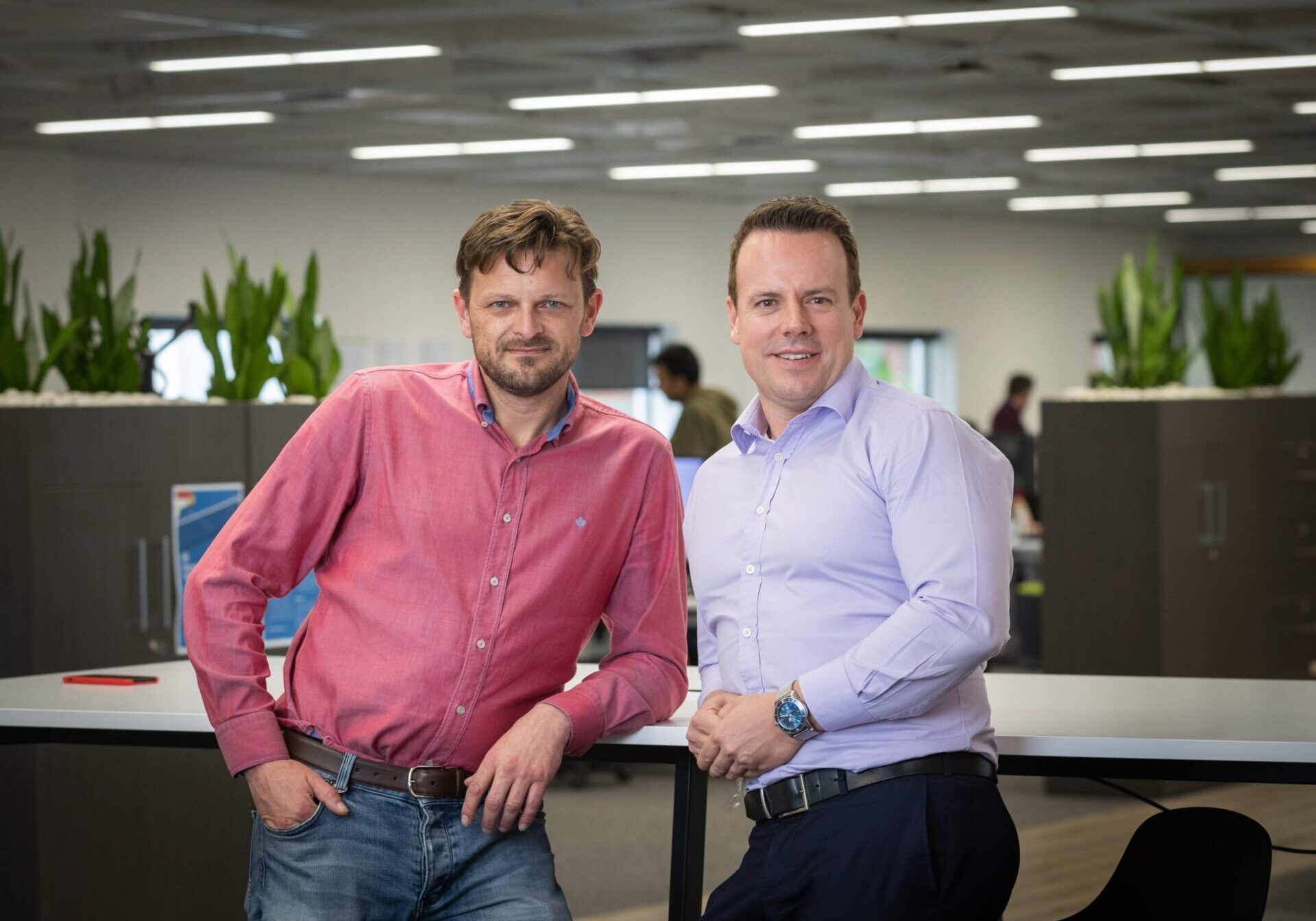 Two men smiling and posing in a modern office space.