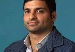 Portrait of a man in a blue jacket against a teal background.