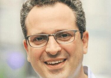 Smiling man with glasses in a casual outdoor setting.