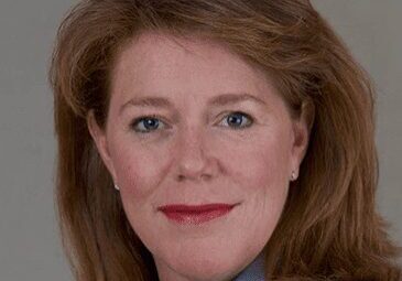 Professional headshot of a middle-aged woman with reddish-brown hair.