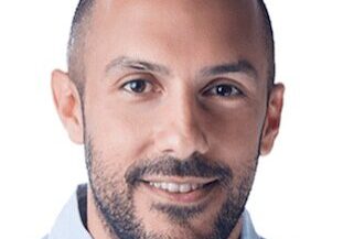 Portrait of a smiling man with a trimmed beard and light blue shirt.