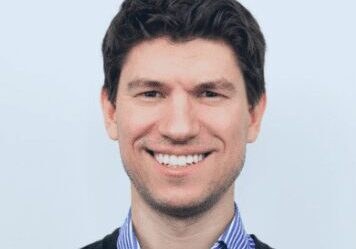 Smiling man in a suit with a light blue background.