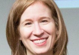 A smiling woman with light brown hair in a casual setting.