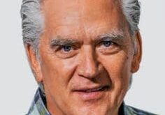 Portrait of an elderly man with gray hair wearing a plaid shirt.