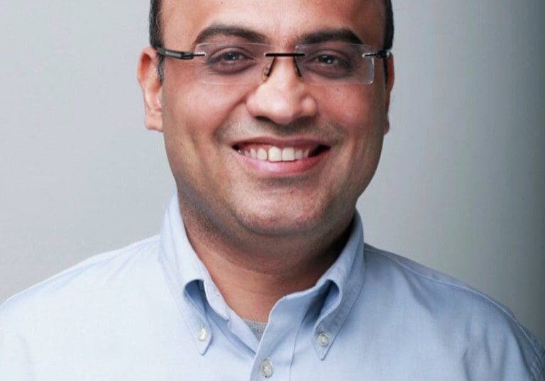 Smiling man wearing glasses and a light blue shirt.