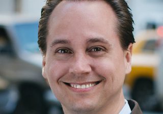 Smiling man in a suit with blurred background.