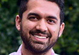 Smiling man with a beard and short hair outdoors.