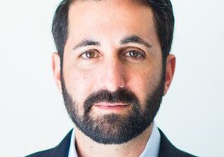 Professional man with dark hair and beard in a suit jacket.