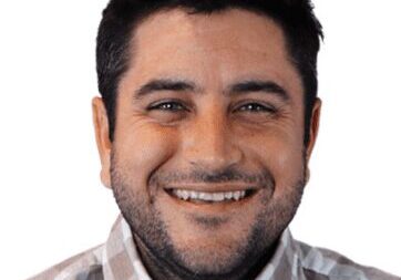 Smiling man with dark hair and a checkered shirt.