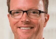 Smiling man with glasses in a professional setting.