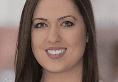 Professional woman with long dark hair smiling at the camera.
