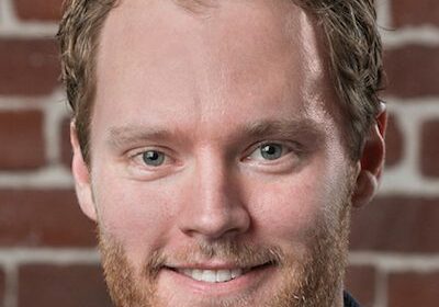 Portrait of a smiling man with curly brown hair and a beard.