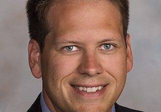 Professional headshot of a smiling man in a suit and tie.