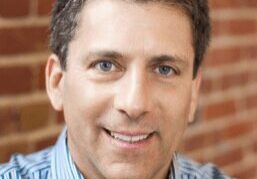 Smiling man with short brown hair in a blue striped shirt.