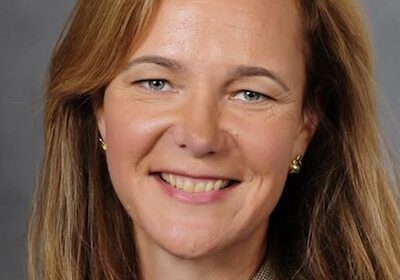 A smiling woman with light brown hair and a gray blazer.