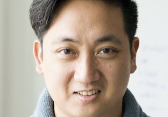 Portrait of a smiling young man with dark hair and a gray sweater.