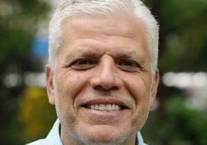 Smiling elderly man with white hair outdoors.