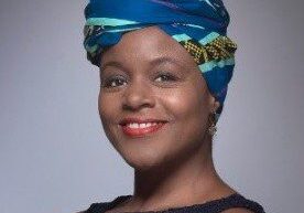 Smiling woman wearing a blue patterned headwrap and dark top.