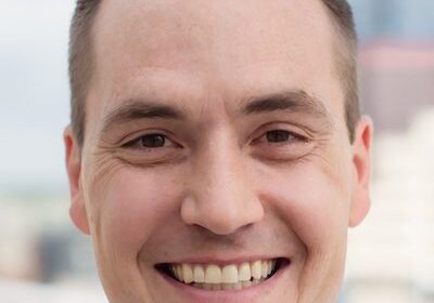 Smiling man with short hair in an outdoor setting.