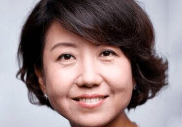 Portrait of a smiling woman with short dark hair against a gray background.