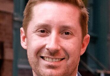 Smiling man with light brown hair in a suit jacket.